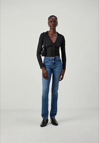Černý dlouhý rukáv top se zapínáním na knoflíky, kombinovaný s modrými džíny. Modelka má na sobě černé boty a nese malou černou kabelku.