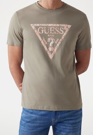 Olive green cotton t-shirt with a triangular white and metallic rose gold "GUESS" logo graphic on the chest; crew neckline, short sleeves.