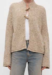 Beige stickad cardigan med ett texturerat mönster, med en ribbad krage och träspännen framtill. Löst passform, kort längd.