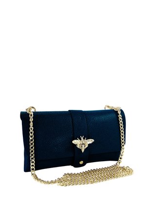 Schwarze, strukturierte Clutch mit goldfarbenem, bienenförmigem Verschluss und langem goldfarbenem Kettenriemen, der daneben auf weißem Hintergrund aufgewickelt ist.