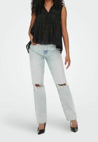 Mustat hihattomat puserot, joissa on pleattiliike, yhdistettynä vaaleansinihin revittyihin farkkuihin ja mustiin korkokenkiin, esittelee rentoa asukokonaisuutta.