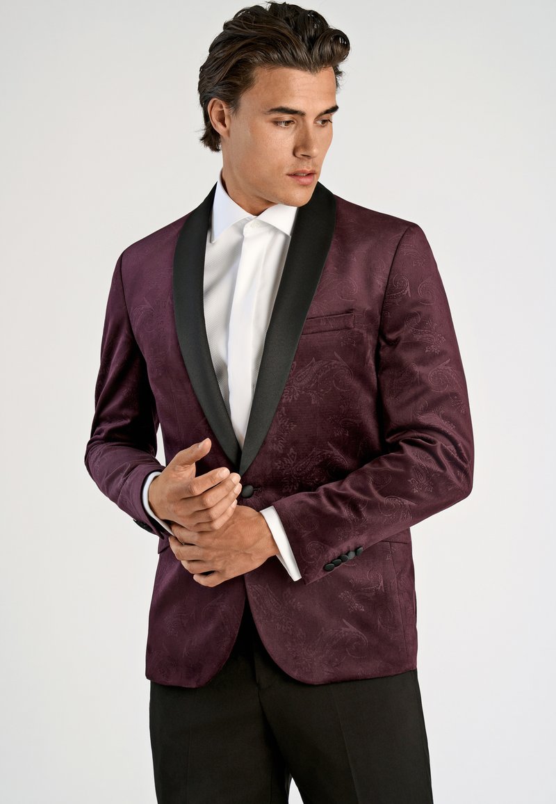 Burgundimönstrad kavaj med svart satin sjalkrage, en ficka och två knappar, i kombination med en vit skjorta och svarta byxor.