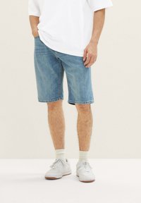 Pantalones cortos de mezclilla en azul claro, con un corte recto, dobladillo deshilachado y diseño clásico de cinco bolsillos, llevados con zapatillas blancas y calcetines hasta el tobillo.