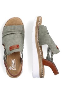 Sandales en cuir vert avec une texture en daim doux, semelle en caoutchouc blanche et accents en cuir brun. Comprend des coutures décoratives et le logo de la marque.