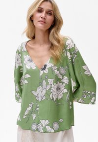 Zielona bluzka z głębokim dekoltem w kształcie V, długimi rękawami i białymi kwiatowymi wzorami. Wykonana z lekkiego materiału, ma luźny krój i obniżony dół.