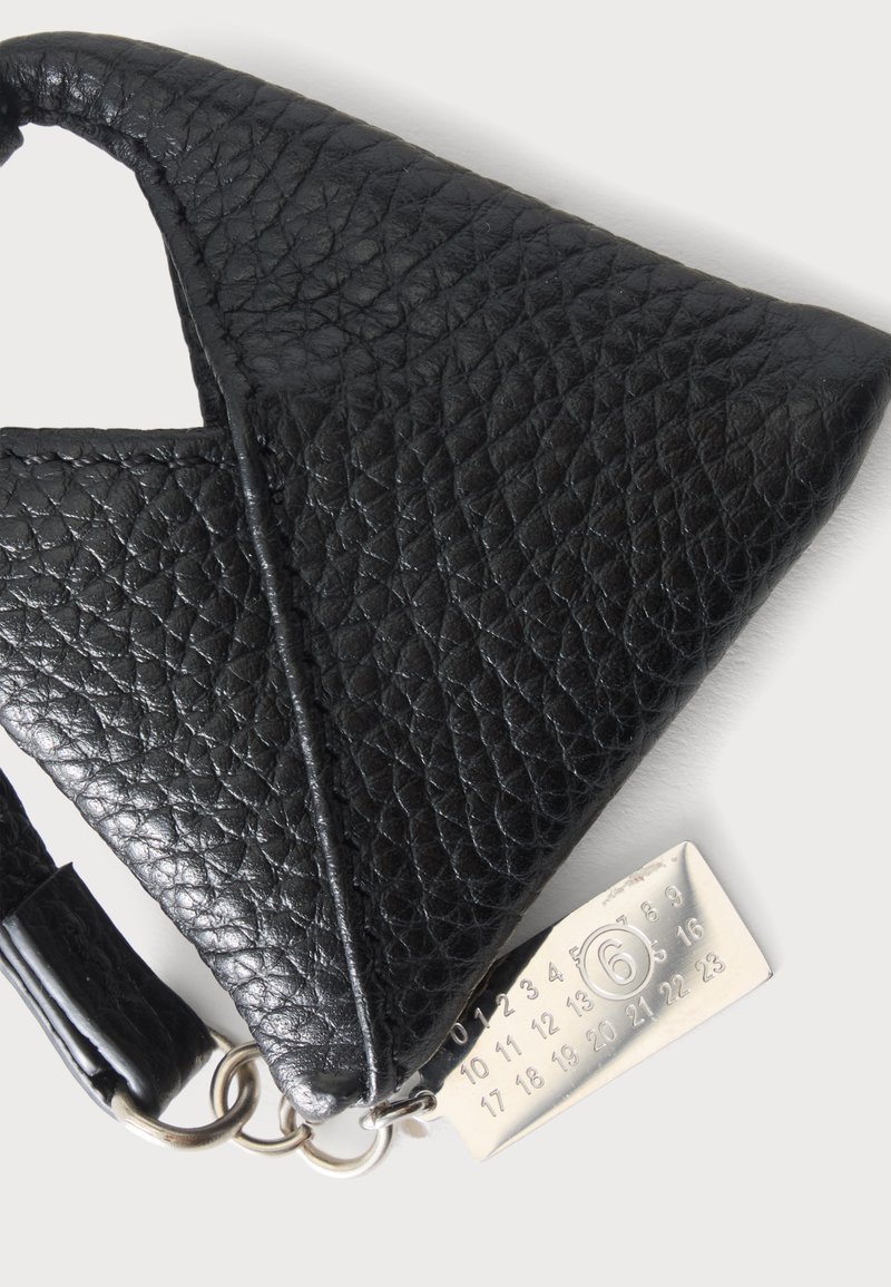 Coin d’un sac à main en cuir texturé noir avec une étiquette métallique argentée affichant les numéros de 0 à 23, le numéro 6 étant entouré.
