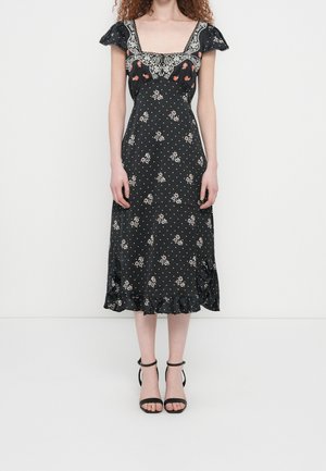 Vrouw draagt een zwarte midi-jurk met witte polkadots, kleine bloemenprints, geborduurde vierkante hals, korte gerimpelde mouwen en zwarte enkellaarzen met hak.