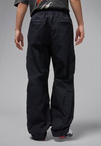 Schwarze Cargo-Hosen mit lockerer Passform, ausgestattet mit mehreren Taschen und einem elastischen Bund, aus strapazierfähigem Material mit glatter Textur.