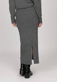 Jupe maxi en tricot côtelé gris avec fente sur le côté, présentant une silhouette ajustée et associée à des bottes à talons noires.