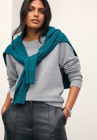 Gray sweater with ribbed cuffs, paired with black leather pants. A teal knit sweater is draped around the shoulders. Silver bracelet accent.