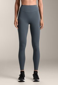 Hochtaillierte, enganliegende Leggings in einem gedämpften Grauton mit glattem Texture. Sie verfügt über einen nahtlosen Bund und wird mit schwarzen Turnschuhen ergänzt.