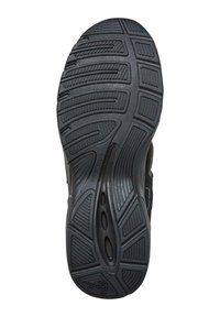 Semelle en caoutchouc noir avec des motifs de relief texturés, présentant des rainures courbes, des découpes circulaires et un logo dans la zone du talon.