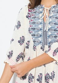 Hvid tunika med blomsterbroderi i navy og pink. Har en nøglehul_front, samlede ærmer og en flæset kant. Blød tekstur.
