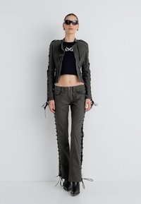 Must musta crop top, vormitud roheline nahkjakk küljele paeltega ja lahvatuvad rohelised püksid paeltega, kombineeritud mustade kontsakingadega.