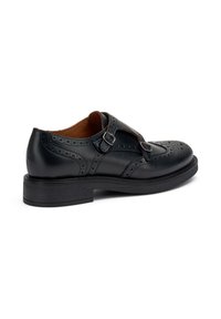 Zapato de cuero negro con diseño de tiras en T, detalles de brogue y dos hebillas ajustables. Suela negra resistente con un ligero tacón.