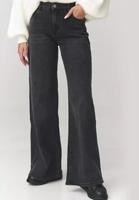 Czarne dżinsowe spodnie z rozszerzanymi nogawkami i wysokim stanem, wykonane z denimu, charakteryzują się klasycznym pięciopocketowym wzornictwem oraz subtelnym przetarciem wzdłuż nogawek.