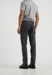 Black denim jeans with a straight cut, featuring a mid-rise waist and back pockets. Worn with a grey short-sleeve shirt and black boots.