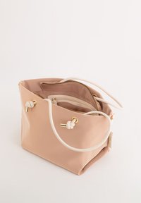 Pehmeä vaaleanpunainen synteettinen kassi, jossa on valkoiset köysikahvat, kultaiset yksityiskohdat ja vetoketjulla varustettu sisätasku. Kassissa on tilava muotoilu ja solmittuja yksityiskohtia.