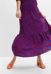 Abito midi con motivo floreale blu e rosso con orlo a volant, abbinato a mules con tacco a blocco arancioni. L'abito presenta un corpetto aderente e maniche ampie.