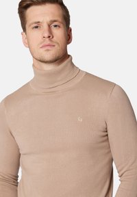 Beżowy sweter z golfem wykonany z dzianiny prążkowanej, z małym haftowanym logo na piersi i dopasowanym krojem.