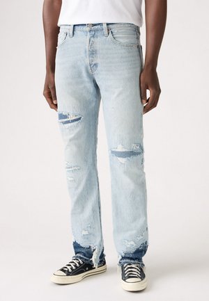 Light blue denim jeans with distressed details, frayed hems, and a relaxed fit. Paired with black canvas sneakers.