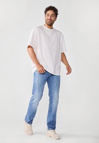 Hvit bomull t-skjorte, løs passform, rund hals; kombinert med lyseblå denimjeans, casual passform. Beige sneakers fullfører antrekket.