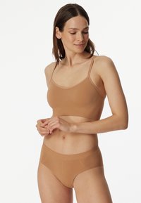 Nude-kleurige naadloze bh en broekset met dunne bandjes en zachte textuur. De bh heeft een eenvoudig ontwerp; de broekjes hebben een comfortabele tailleband.