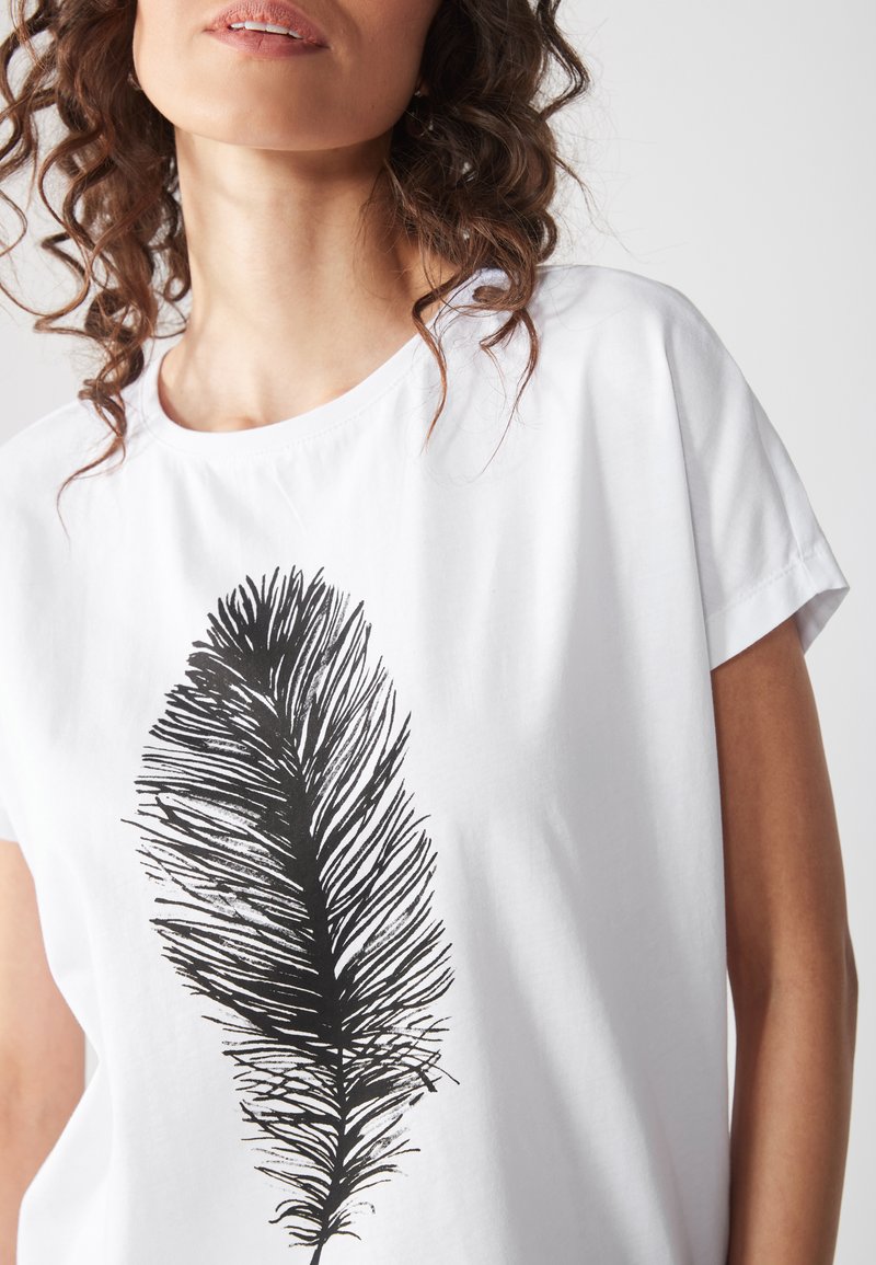T-shirt en coton blanc avec un grand motif graphique de plume noire. Manches courtes et encolure ronde. Texture lisse et coupe décontractée.