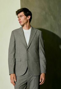 Gray pinstriped blazer with notch lapels, single button closure, side pockets, and textured fabric, paired with a plain white shirt.