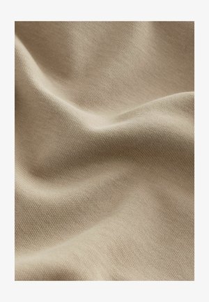 Tessuto di cotone beige che mostra una superficie liscia e strutturata con sottili motivi a maglia, caratterizzato da dolci onde e una caduta morbida.