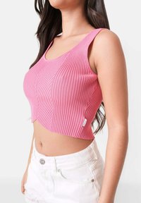 Roosa lühike tank top tekstuurse ribikujundusega ja laiade rihmadega. Koos valgete denimsorte, mis näitavad sobivat stiili ja vormi.