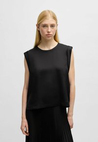 Top nero senza maniche con scollo a giro, texture liscia e vestibilità rilassata, abbinato a una gonna nera plissettata.