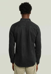 Camicia in denim nera con maniche lunghe, polsini con bottone, colletto classico e orlo curvo, realizzata in un tessuto testurizzato e con dettagli minimi.