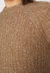 Brązowy sweter z prążkowanym splotem, wykonany z miękkiego materiału, z okrągłym dekoltem i subtelnymi wariacjami kolorystycznymi.