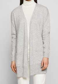 Grå stickad kofta med avslappnad passform, öppen front, långa ärmar och två framfickor. Mjuk textur och ribbade ärmslut.