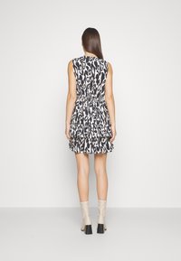 Vestito corto senza maniche in stampa leopardata crema e nera, con vita stretta e orlo a volant stratificato. Completato da stivali al ginocchio beige.