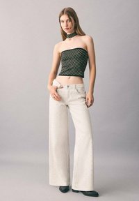 Top sin mangas a rayas negras y verdes, combinado con pantalones anchos blancos con detalles de pliegues y zapatos negros.