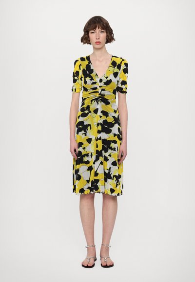 Robe à motifs floraux en jaune, noir et gris. Manches courtes bouffantes, décolleté en V, corsage froncé et jupe fluide avec ourlet festonné.