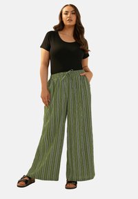 Gröna randiga vidbyxor med elastiskt midjeband och snörning, tillsammans med en svart åtsittande t-shirt och svarta sandaler.