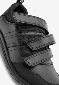 Botte de sport noire avec des sangles Velcro, en cuir lisse et en tissu texturé, bout arrondi et détail de couture contrasté.