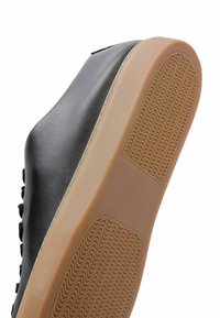 Sneaker in pelle nera con suola in gomma beige strutturata e un motivo ondulato, area delle dita rinforzata. Design con lacci e accenti minimali.