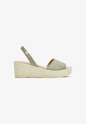 Sandalia de cuña de ante verde con punta abierta, tira trasera y plataforma natural envuelta en yute. Superficie texturizada y diseño minimalista.