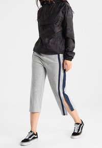 Svart kamouflagemönstrad huvtröja med en framficka, i kombination med ljusgrå avkortade sweatpants med marinblå sidostycken och slitsar. Svarta sneakers.