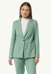 Mint green tailored blazer with two front pockets and a single button closure, made from smooth fabric, paired with a white textured sweater.