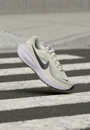 Λευκό και μαύρο παπούτσι για τρέξιμο Nike στον αέρα πάνω από ένα μαύρο-ασπρο διάβαση πεζών με μικρά συντρίμμια γύρω από τη σόλα.