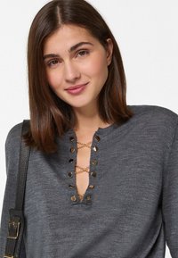 Graues Strickoberteil mit V-Ausschnitt, verziert mit goldfarbener Hardware und einem dekorativen Kreuzstich-Lace-Detail. Strukturiertes Material und Schulternähte.