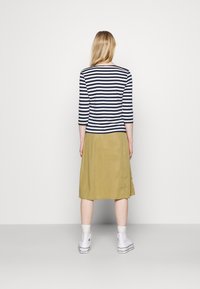 Randig navy och vit långärmad topp i kombination med en enfärgad olivgrön kjol, avslutad med vita högskor. Minimalistisk design.