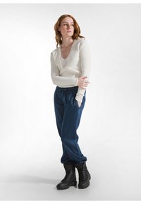 Helles beige, geripptes Langarmoberteil, kombiniert mit lockeren blauen Jeans und schwarzen Schnürstiefeln. Das Oberteil hat ein einzigartiges, geknotetes Design an der Taille.