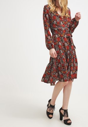 Langärmeliges Wickelkleid in Schwarz mit rotem Blumenmuster, mit mehrstufigem Rock und Taillenbindung. Kombiniert mit schwarzen Sandaletten mit Absatz.