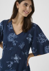 Sötétkék ruha rövid, fodros ujjakkal, világoskék virágmintával. V-alakú kivágás, ráncolt derékkal, texturált anyagból készült.